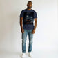 Hustler Design navy blue 100% cotton t-shirt with a graphic print of a car with its door open in a foggy parking lot at night, under a neon diamond sign.